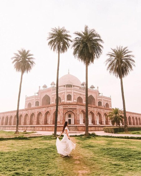 A woman in a white dress walking towards a large, ornate building with a dome, surrounded by palm trees. 5