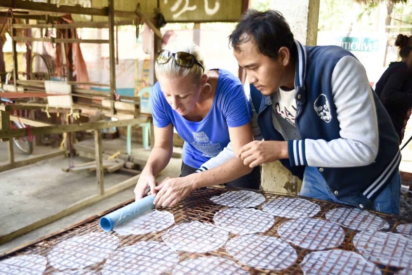 Two people working on a metal grid table, handling a rolled-up material. 1