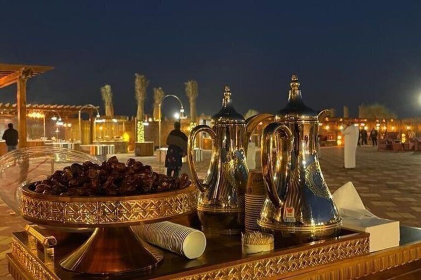 A tray with a bowl of dates, two silver coffee pots, and a teapot on a table at night. 4