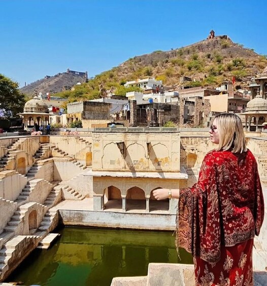 A person in traditional attire overlooking a historic water feature with steps and a hill in the background. 1