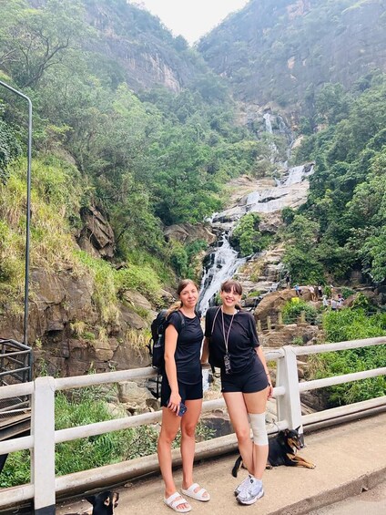 Two people standing by a waterfall in a lush valley. 4