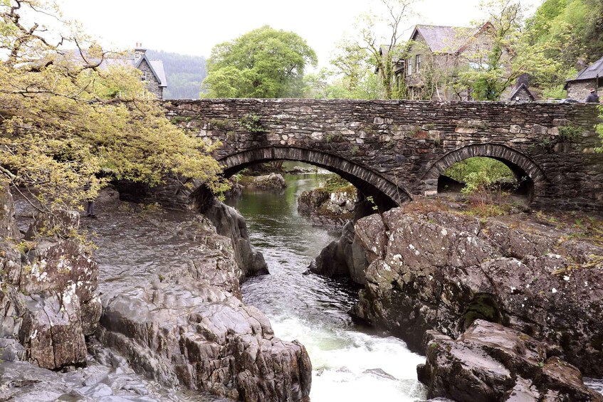 A stone bridge over a flowing river with rocky banks and trees. 2