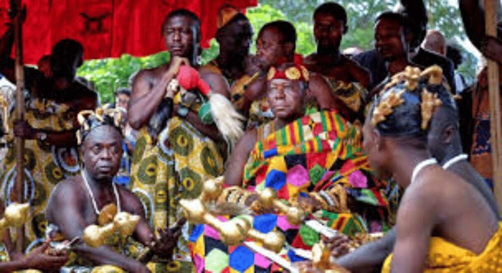 A group of people in traditional attire, some holding objects, in an outdoor setting. 4