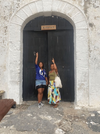 Two people standing in front of a door labeled 'DOOR OF RETURN' with an arched entrance. 5