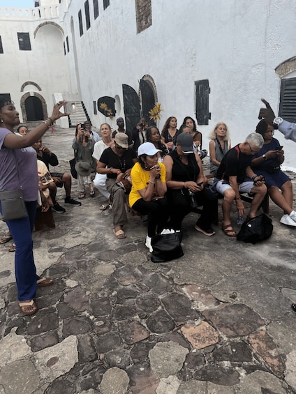 A group of people sitting on a stone-paved street in a historic area with white buildings and arched doorways. 2