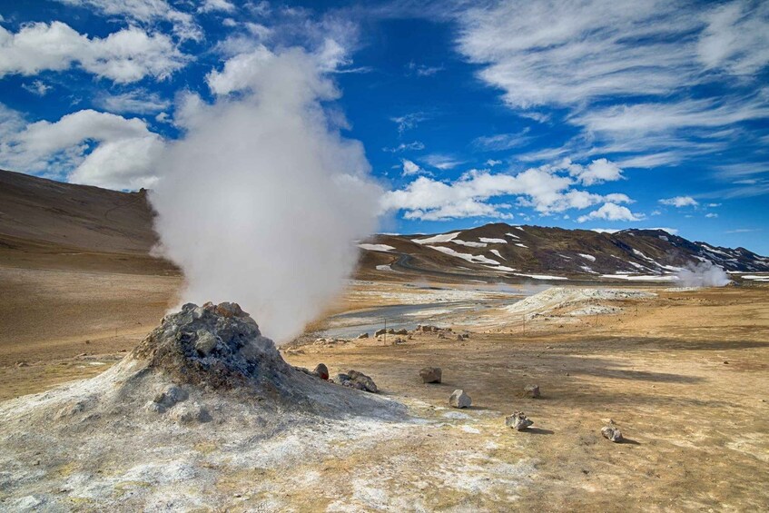A geyser erupting in a dry, mountainous landscape with snow patches and a clear blue sky. 5