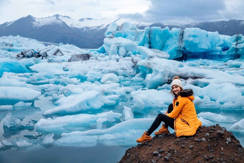 A person sitting on a rocky outcrop surrounded by icebergs in a glacial landscape. 1