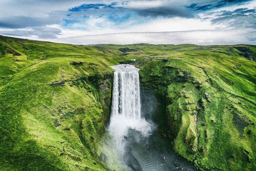 A waterfall in a green valley with a stone structure at the top. 4