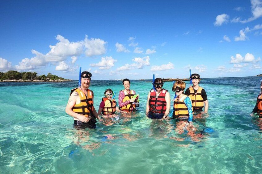 A group of people in clear water with snorkels, wearing life jackets. 2