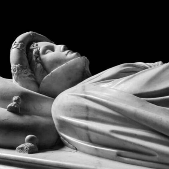 A marble statue of a reclining figure with detailed carvings and a small figure beside it. 4