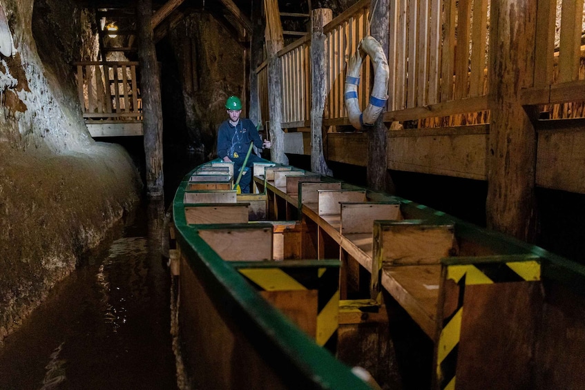 A person in a hard hat and safety vest inside a wooden mine tunnel with wooden benches and a ladder. 4