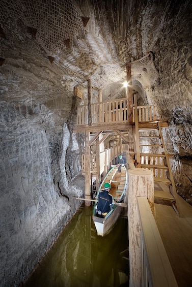 A wooden boat on a narrow waterway inside a cave with wooden walkways and a netted ceiling. 3