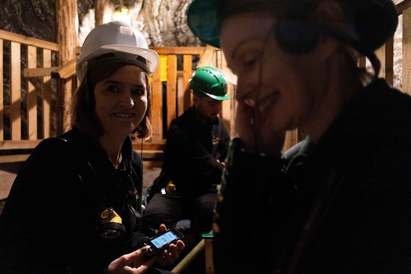People in hard hats and safety gear, one holding a smartphone, in a dimly lit tunnel. 5
