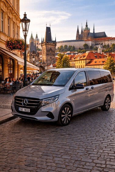 A silver Mercedes-Benz van parked on a cobblestone street in a historic European town with notable architecture in the background. 2