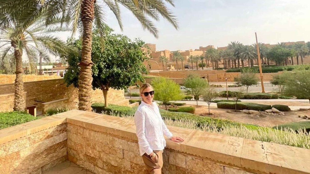 A person standing on a stone wall overlooking a landscaped area with palm trees and a distant cityscape. 5