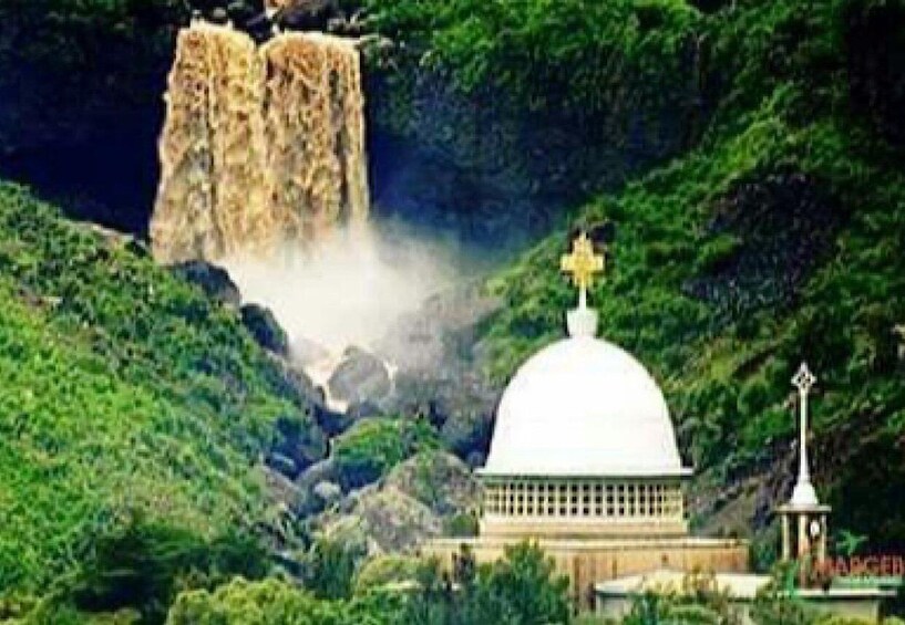 A white dome structure with a cross on top, surrounded by lush greenery and a waterfall in the background. 3