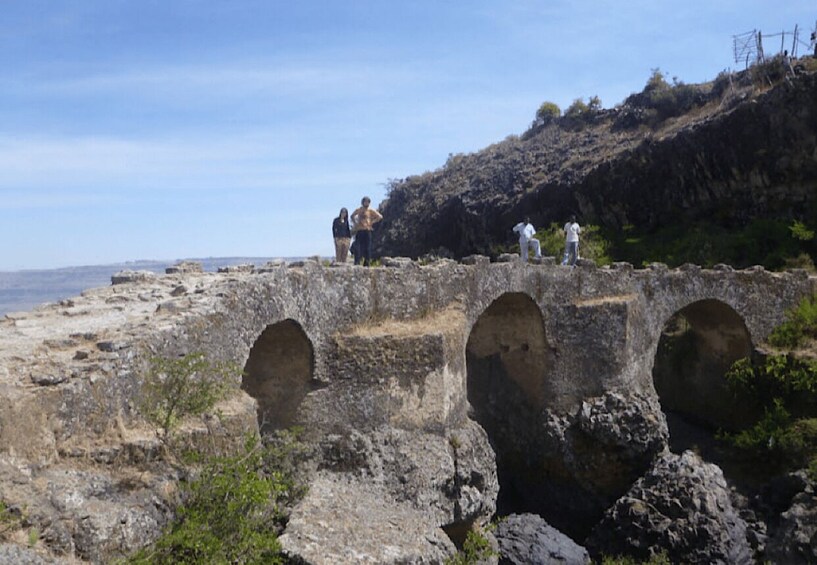 A stone bridge with three arches over a rocky landscape. 2