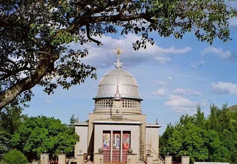 A large, domed building with a spire, surrounded by trees and greenery. 1