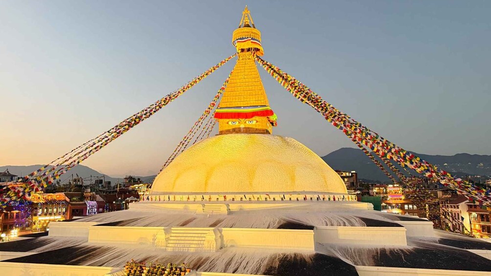 Suuri, kultainen stupa, jonka ympärillä on värikkäitä ruksalipuja, ja jota reunustavat vesi ja rakennukset. 1