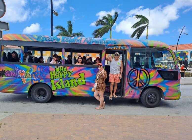 A colorful bus with 'Escape Island Adventures' and 'One Happy Island' graphics, parked on a street with palm trees and buildings in the background. 2