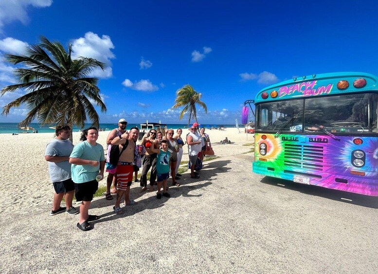 A group of people on a beach with a colorful bus labeled 'Beach Bum' parked nearby. 1