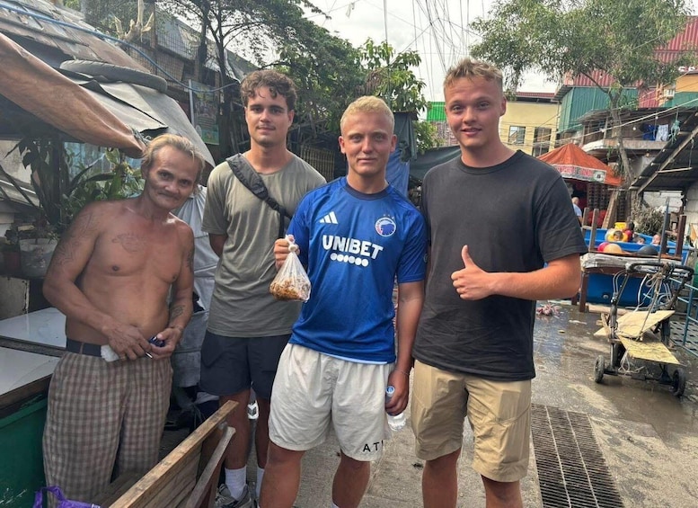 Four men standing outdoors, one wearing a blue sports jersey, another in a grey shirt, and two in casual attire. 1
