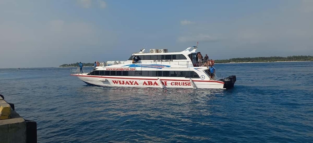 Ein weißes Boot mit roten und blauen Akzenten, genannt 'WIJAYA ABA CRUISE', auf ruhiger See. 1