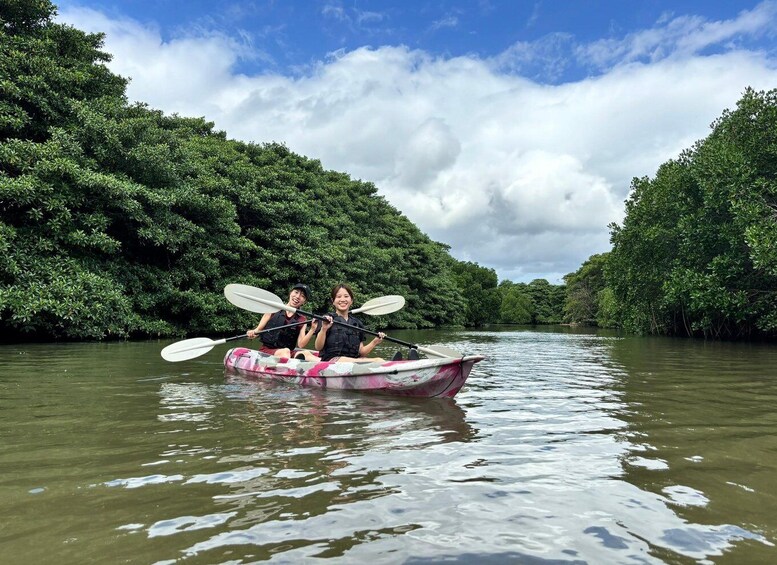 Two people kayaking on a river surrounded by dense green foliage. 3