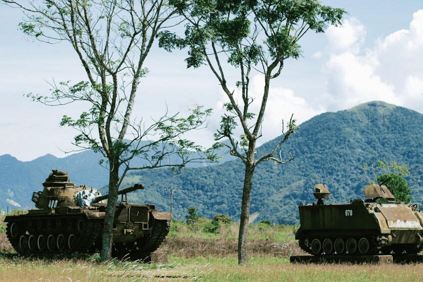 Two military tanks in a field with mountains in the background. 1