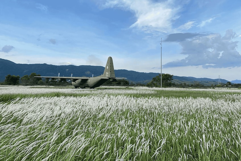 A military aircraft parked in a field with mountains in the background. 2