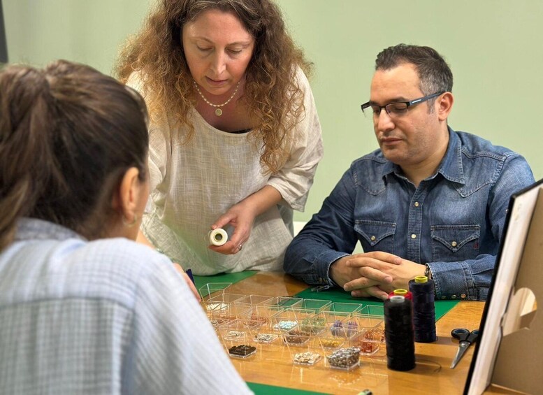 Three people at a table with various craft supplies, including spools of thread and small containers of beads. 1