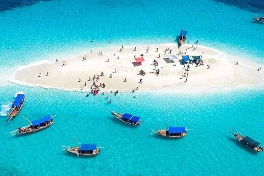 A tropical island with clear turquoise waters, a sandy beach, and several boats anchored near the shore. 2