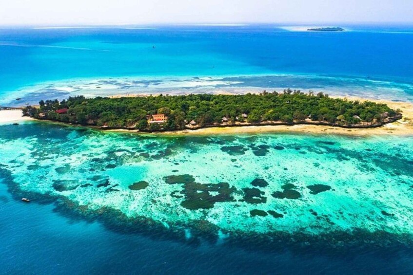 An aerial view of a tropical island with clear turquoise waters, dense green vegetation, and a few buildings. 1