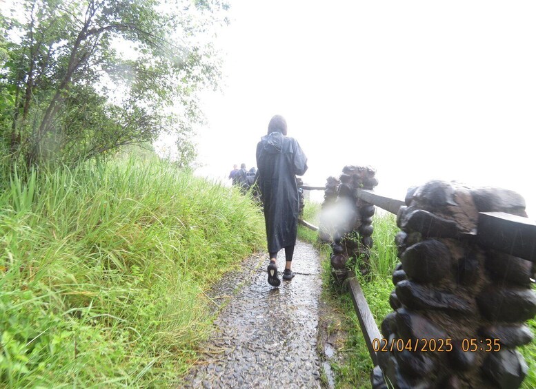 A person walking on a wet path with a stone wall on one side. 5