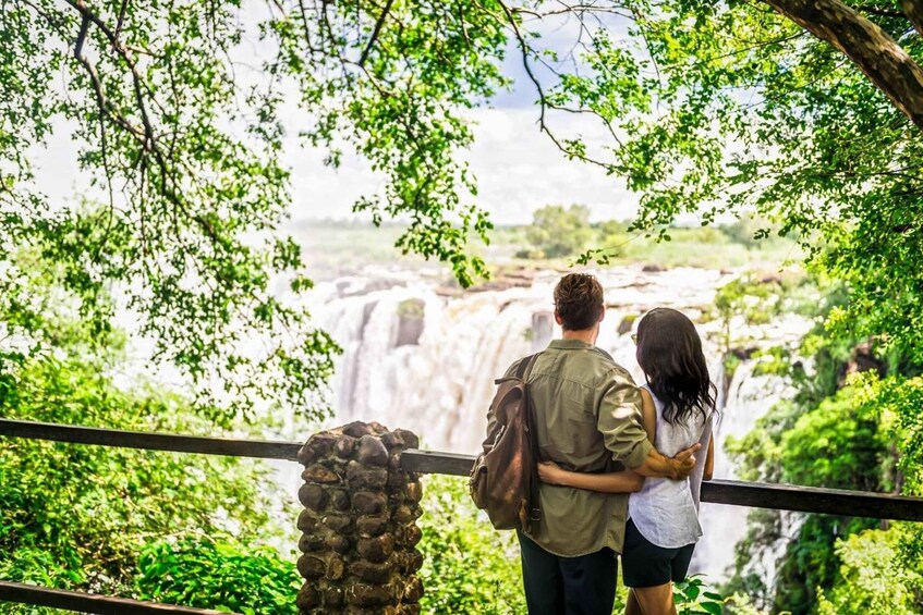 A couple standing by a railing, overlooking a waterfall surrounded by lush greenery. 2