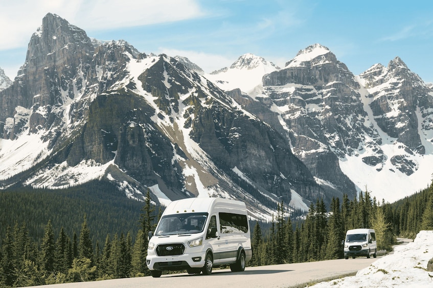 A white RV driving on a snow-covered mountain road with rugged peaks in the background. 4