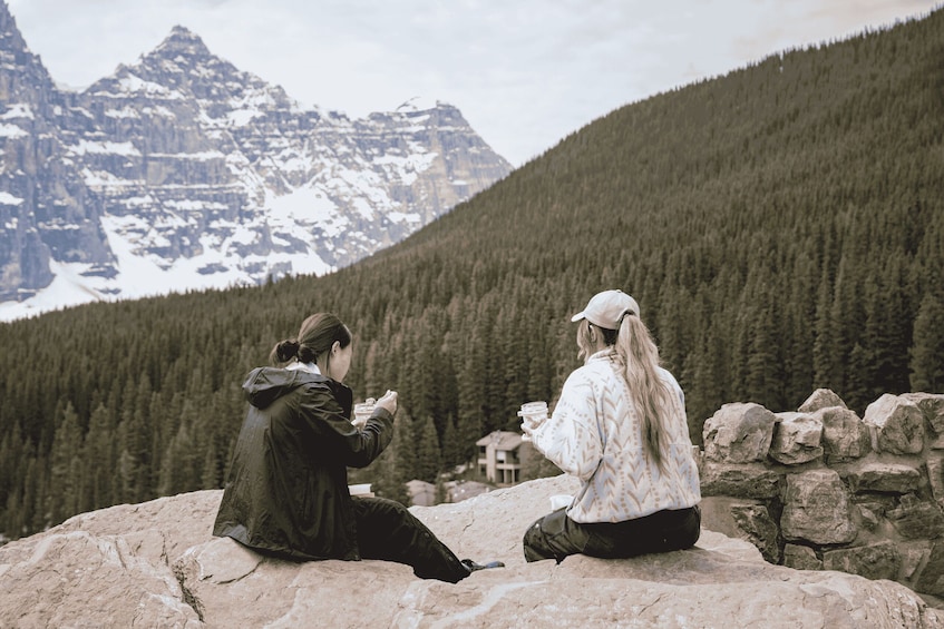 Two people sitting on a rock with a mountainous landscape in the background. 3