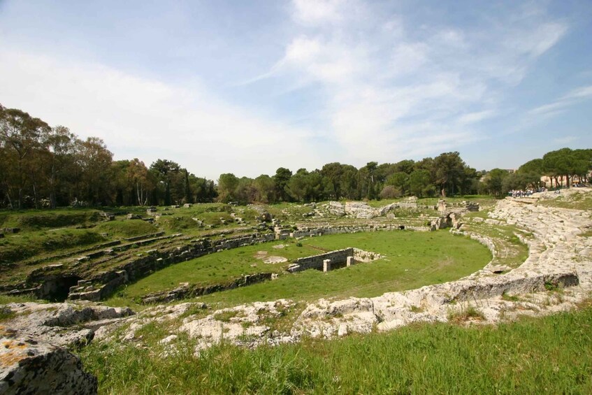 Ancient ruins with stone structures and a circular amphitheater surrounded by grass and trees. 1