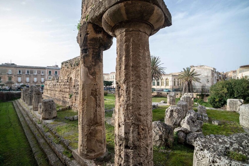 Ancient stone columns and ruins in a historical site with modern buildings in the background. 3
