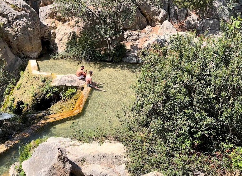 A natural pool surrounded by rocks and vegetation. 3