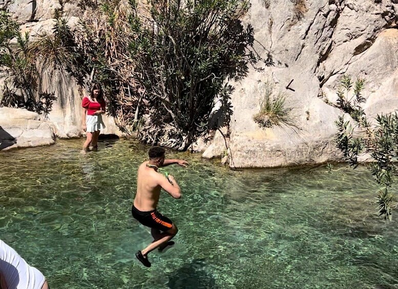 A person jumping into clear water near rocky terrain with sparse vegetation. 1