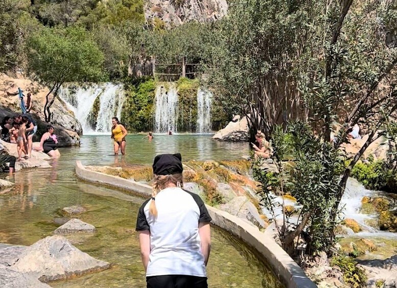 A natural hot spring with multiple waterfalls and people swimming and relaxing. 4