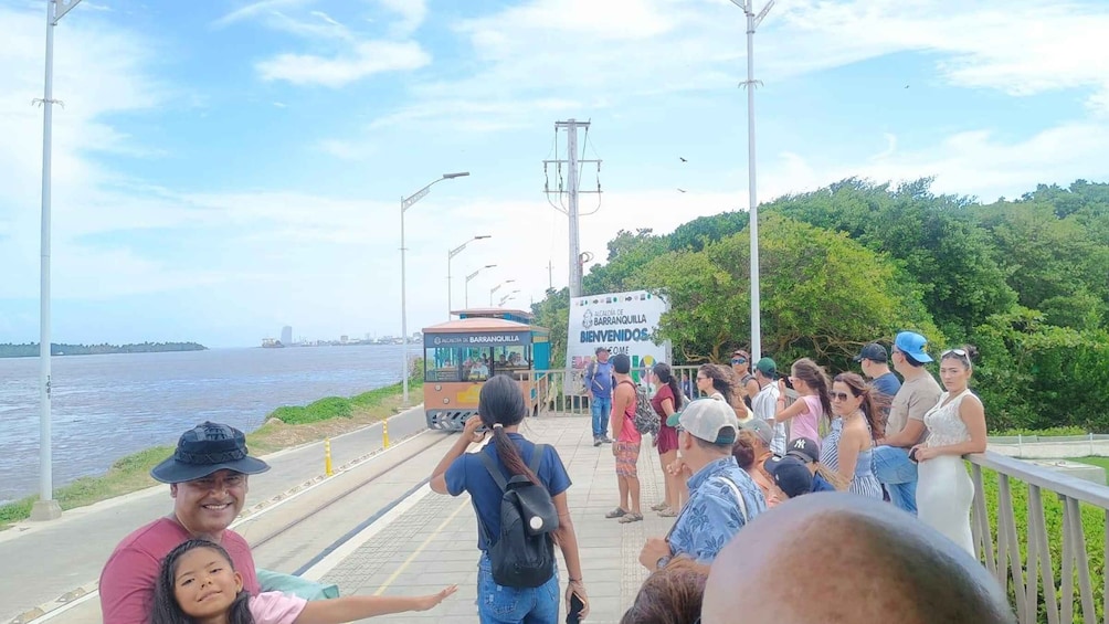 A ferry dock with people waiting, a ferry, and a sign welcoming visitors. 1