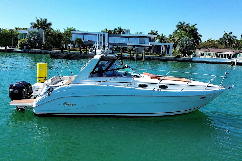 A white motorboat named 'Rinker' docked at a marina with a clear blue sky and palm trees in the background. 1