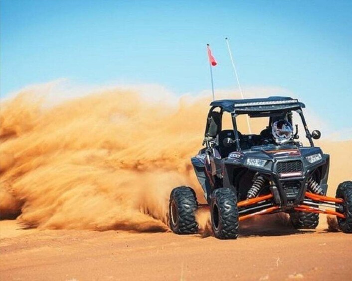 A black off-road vehicle with orange suspension and a red flag on top, driving through a sandy desert. 5