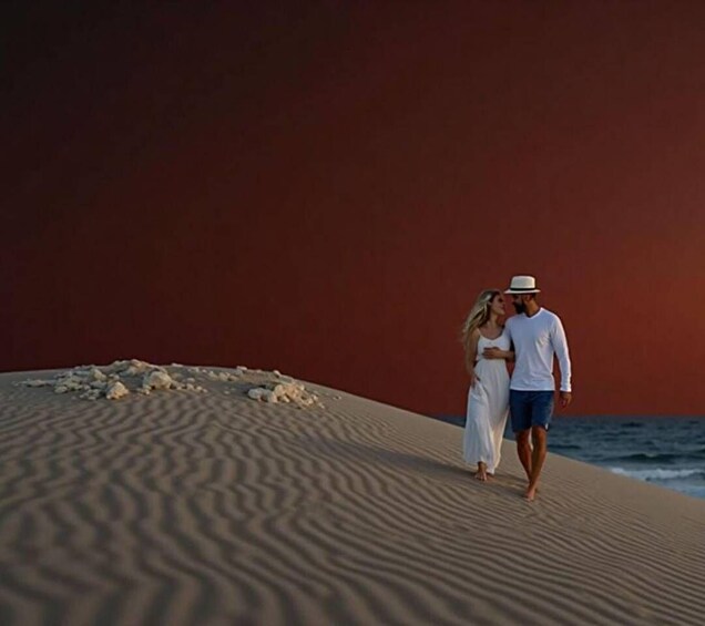 A couple walking on a sandy beach with a red sky. 2