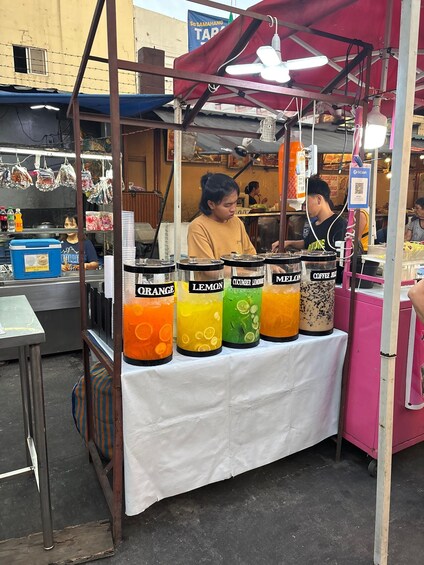 A street food stall with a variety of colorful drinks in large containers. 5