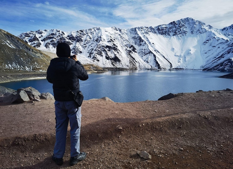 A person taking a photo of a glacier lake with mountains in the background. 5