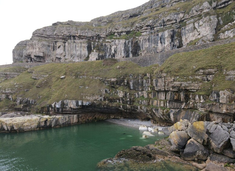A coastal cliff with layered rock formations and a calm greenish sea. 5