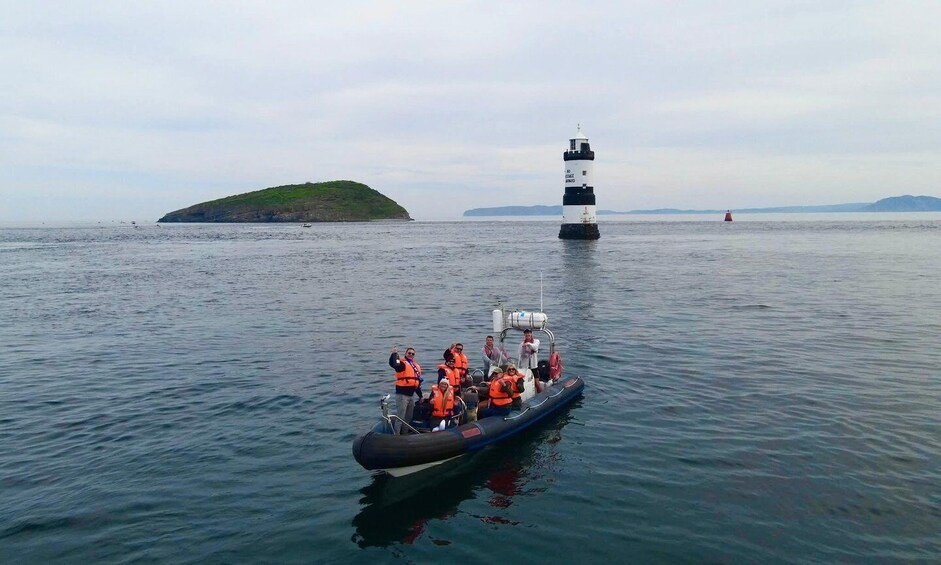 A boat with people wearing life jackets on calm water, a lighthouse in the background, and a small island to the left. 1
